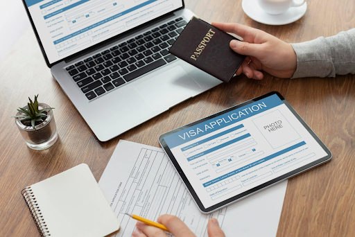 Student completing online visa application with passport, tablet, and laptop on a desk